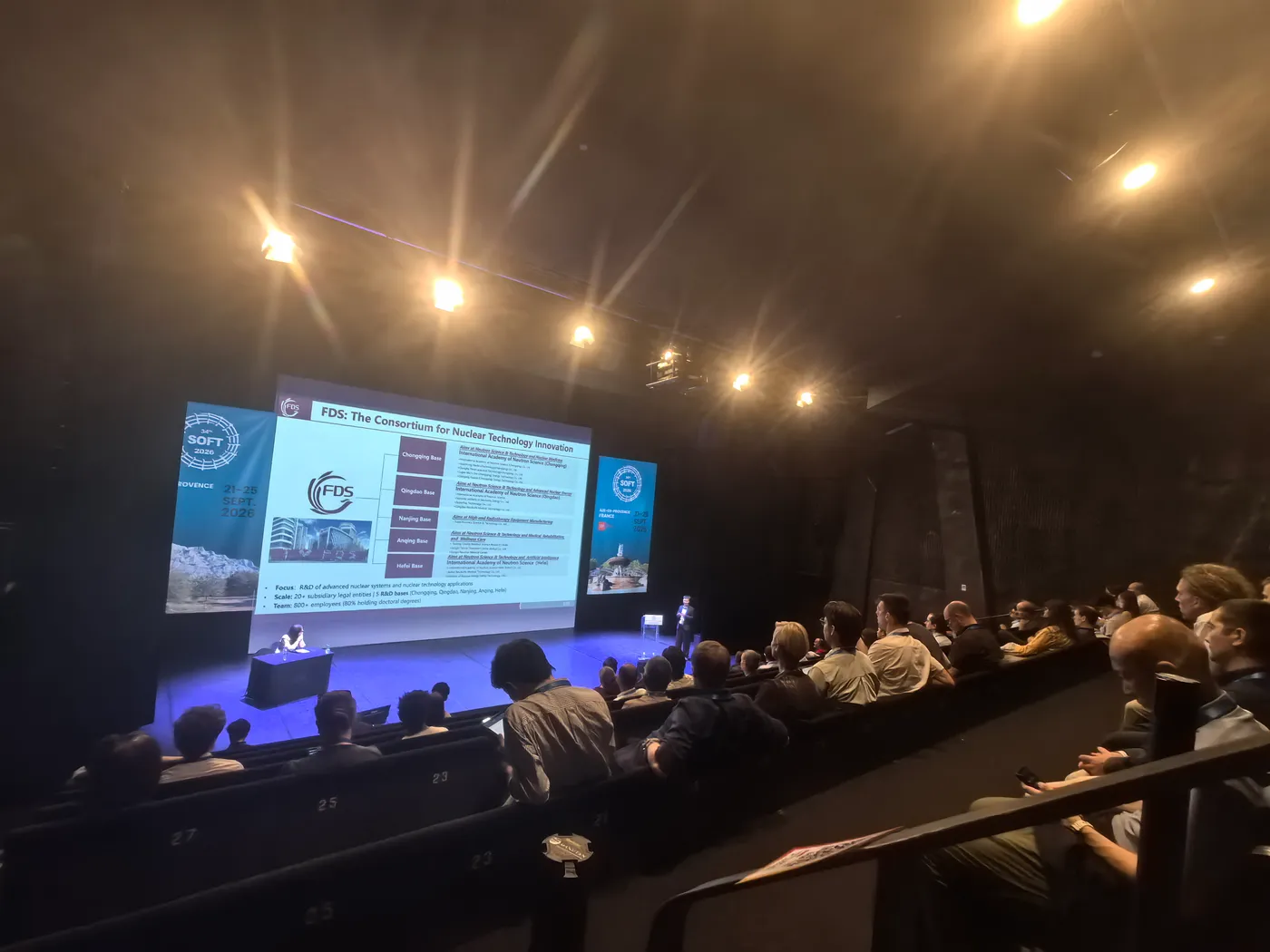 YAO Dong presenting the TopMC talk on stage at SOFT 2026 in Aix-en-Provence, with the FDS Consortium slide on screen